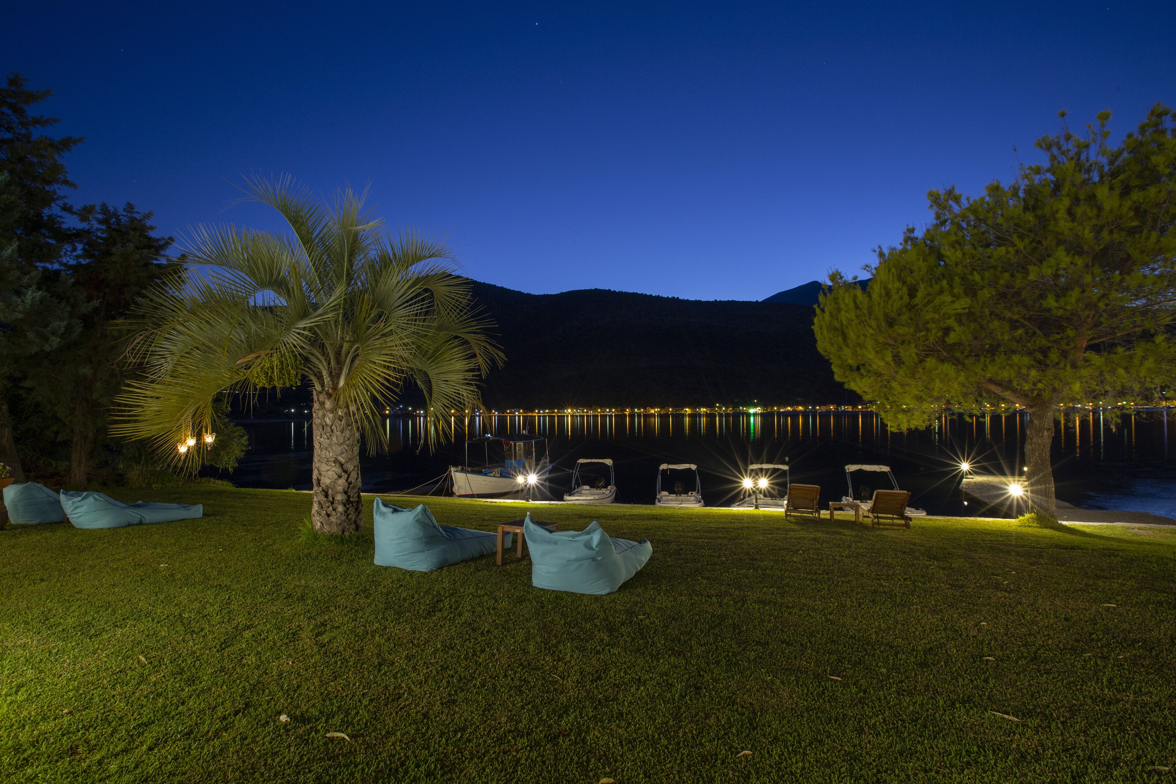 A nighttime outdoor seating area with chairs and bean bags, a palm tree, and a building in the background.