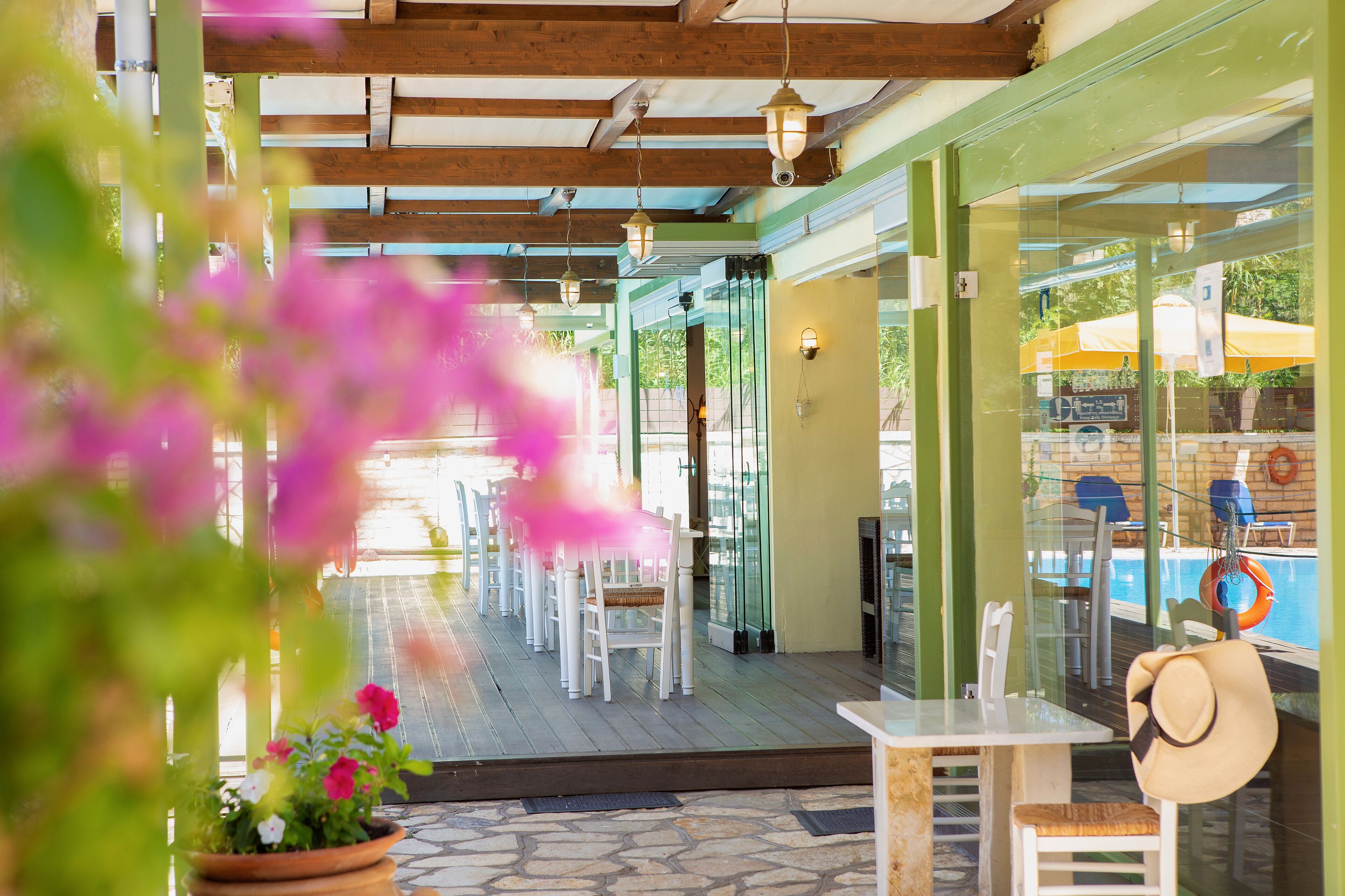 An outdoor patio with white tables and chairs, a pool area visible through glass doors, and a life ring hanging on the glass.