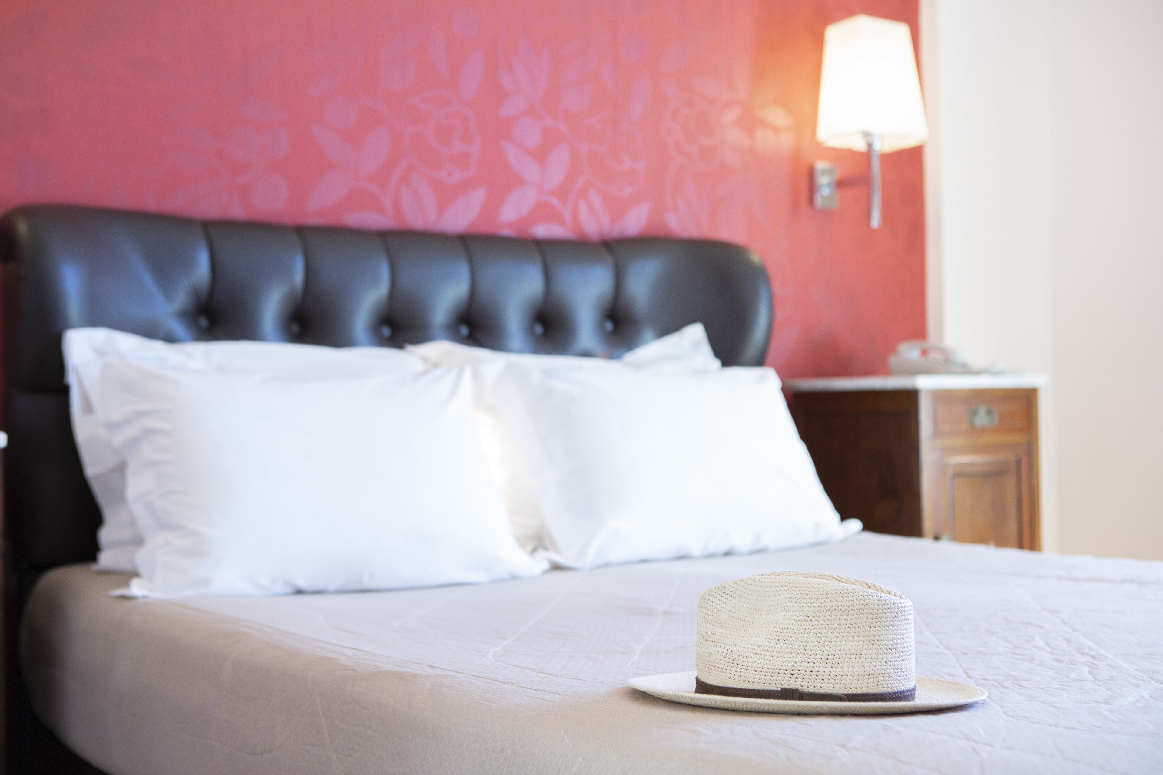 Uma cama com roupa de cama branca, cabeceira preta e um chapéu branco sobre a cama.