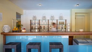 A bar area with a wooden counter, shelves with bottles, and wicker bar stools. - Cleopatra Beach Hotel (Lefkada)
