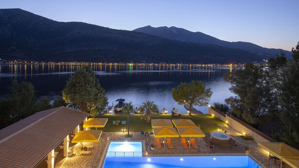 A pool area with lounge chairs and umbrellas, a hot tub, and a view of a lake with mountains in the background. - Cleopatra Beach Hotel (Lefkada)