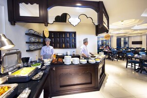 Un buffet avec plusieurs points de service, une grande variété de plats et un espace où les convives peuvent s’asseoir à des tables et sur des chaises.