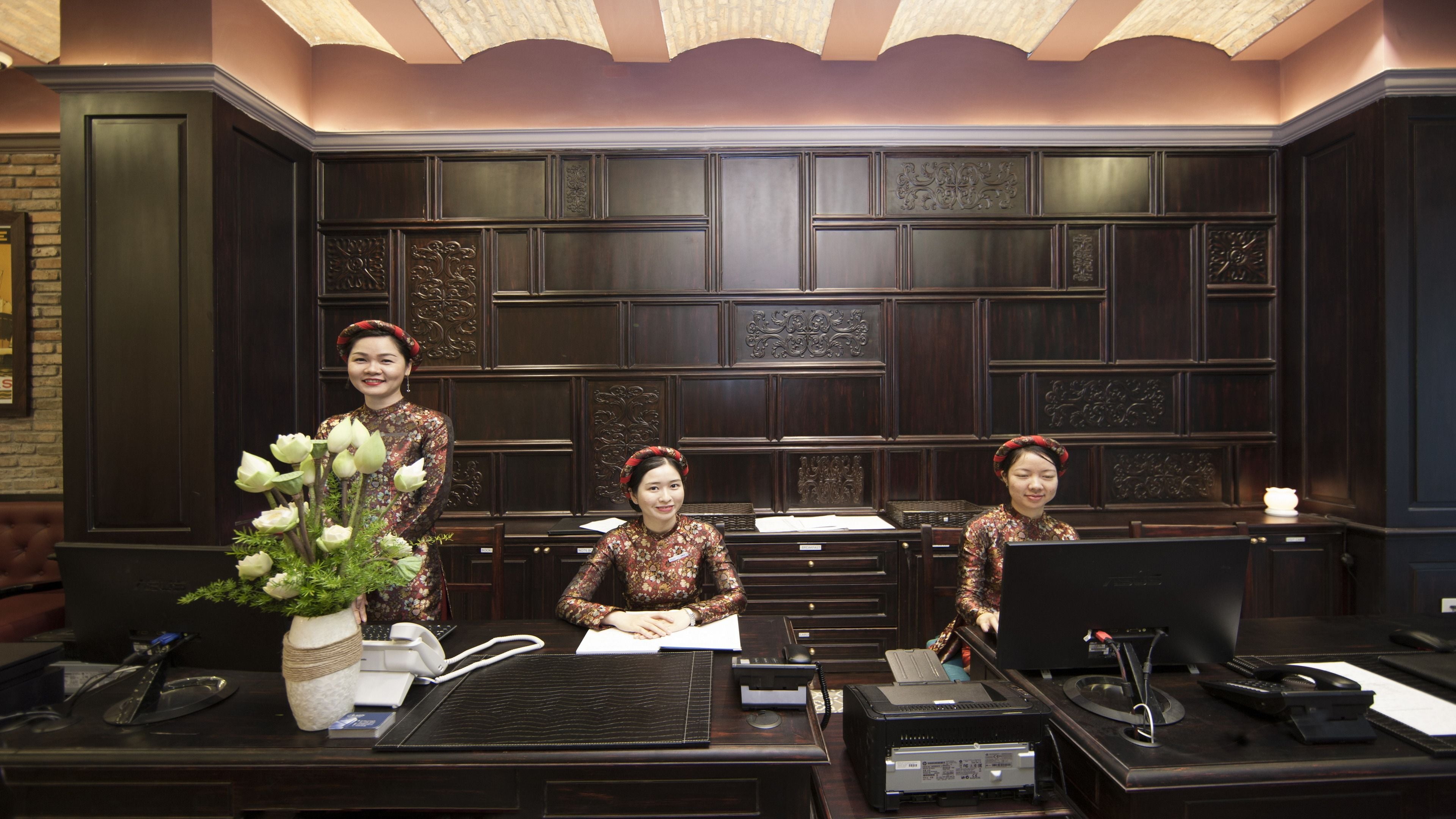 A reception desk with three staff members, a vase of flowers, and various office equipment.