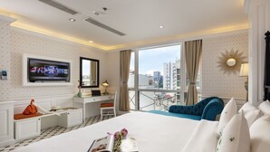 A hotel room with a large bed, a desk with a chair, a TV mounted on the wall, and a balcony with a view of the city.