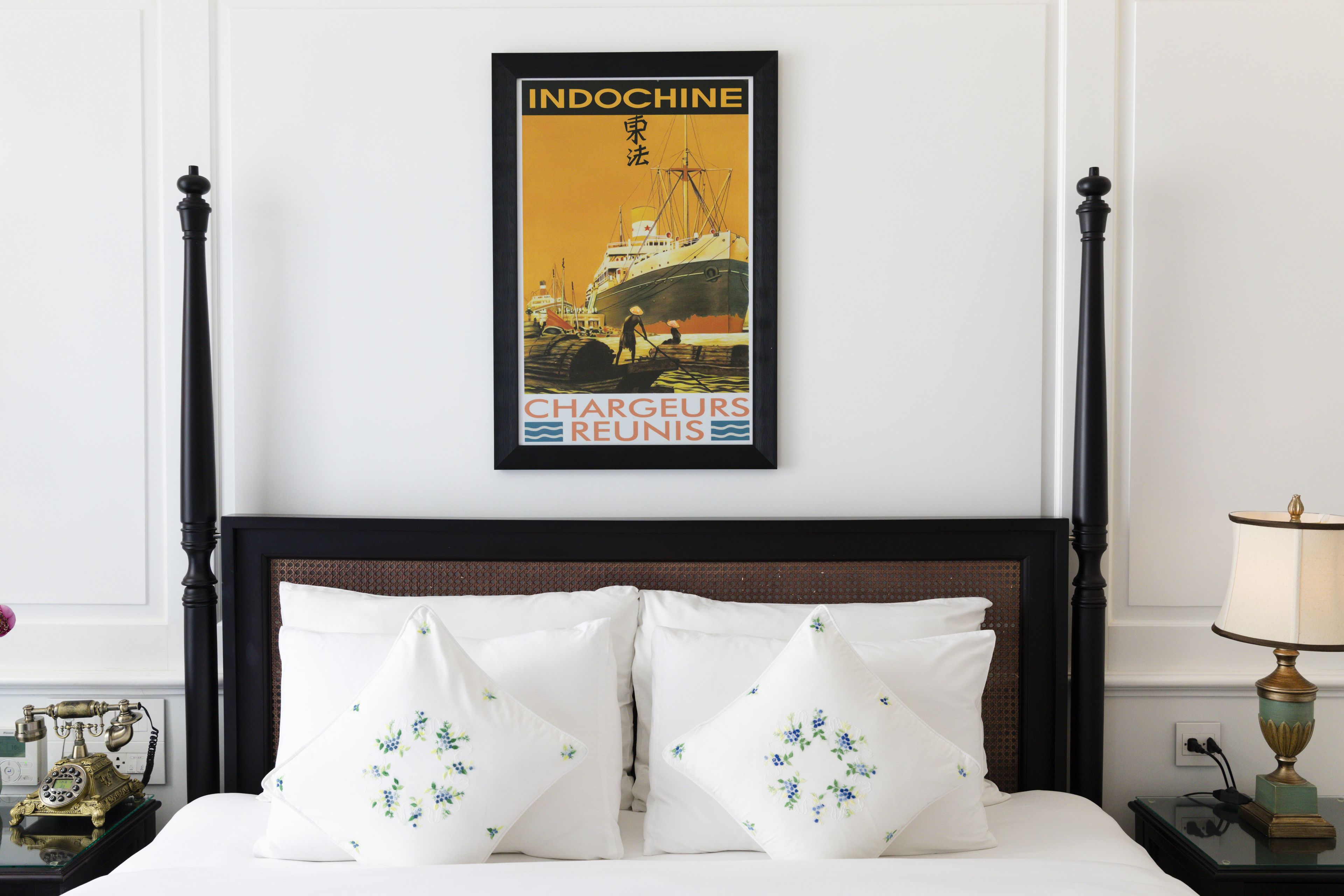 A hotel room with a bed, a nightstand, a lamp, and a poster on the wall.