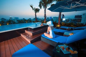 A poolside area with a view of the city skyline, a lounge with blue cushions, and a table with food and drinks. - Alagon D'antique Hotel & Spa (Ho Chi Minh City)