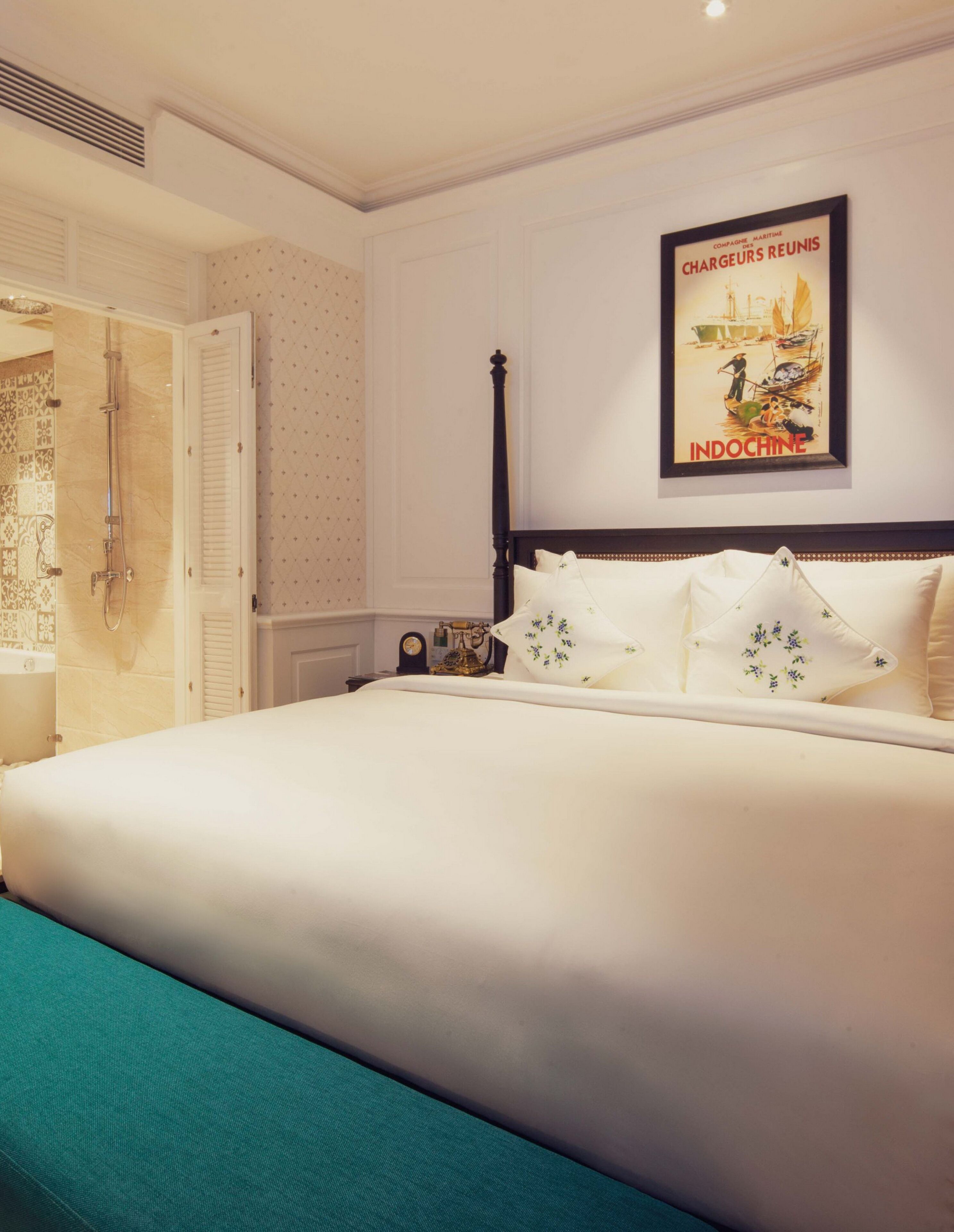 A neatly arranged hotel room with a large bed, a shower, and a wall-mounted poster.
