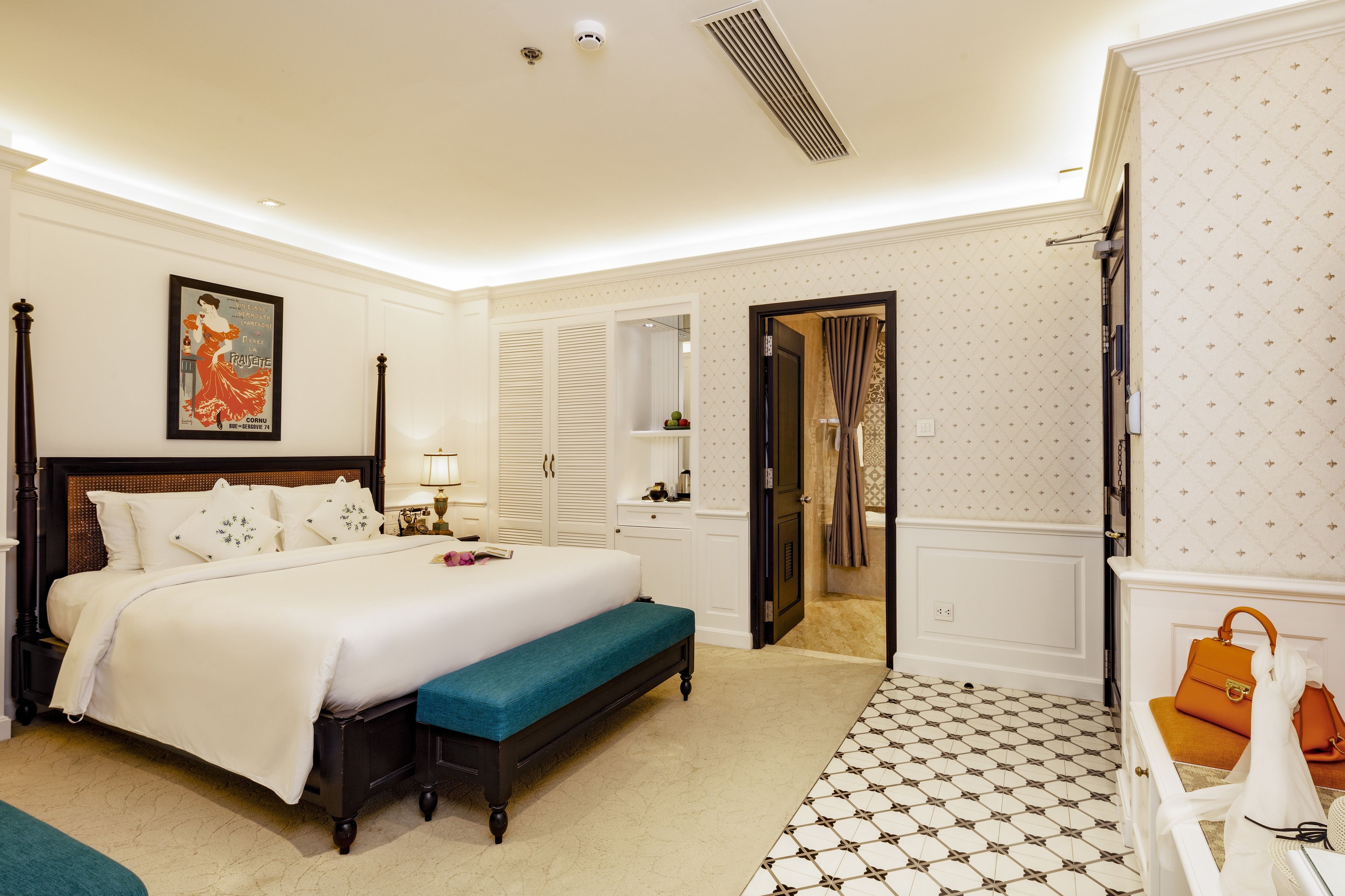 A spacious bedroom with a large bed, a bench, a wardrobe, and a bathroom visible through an open door.