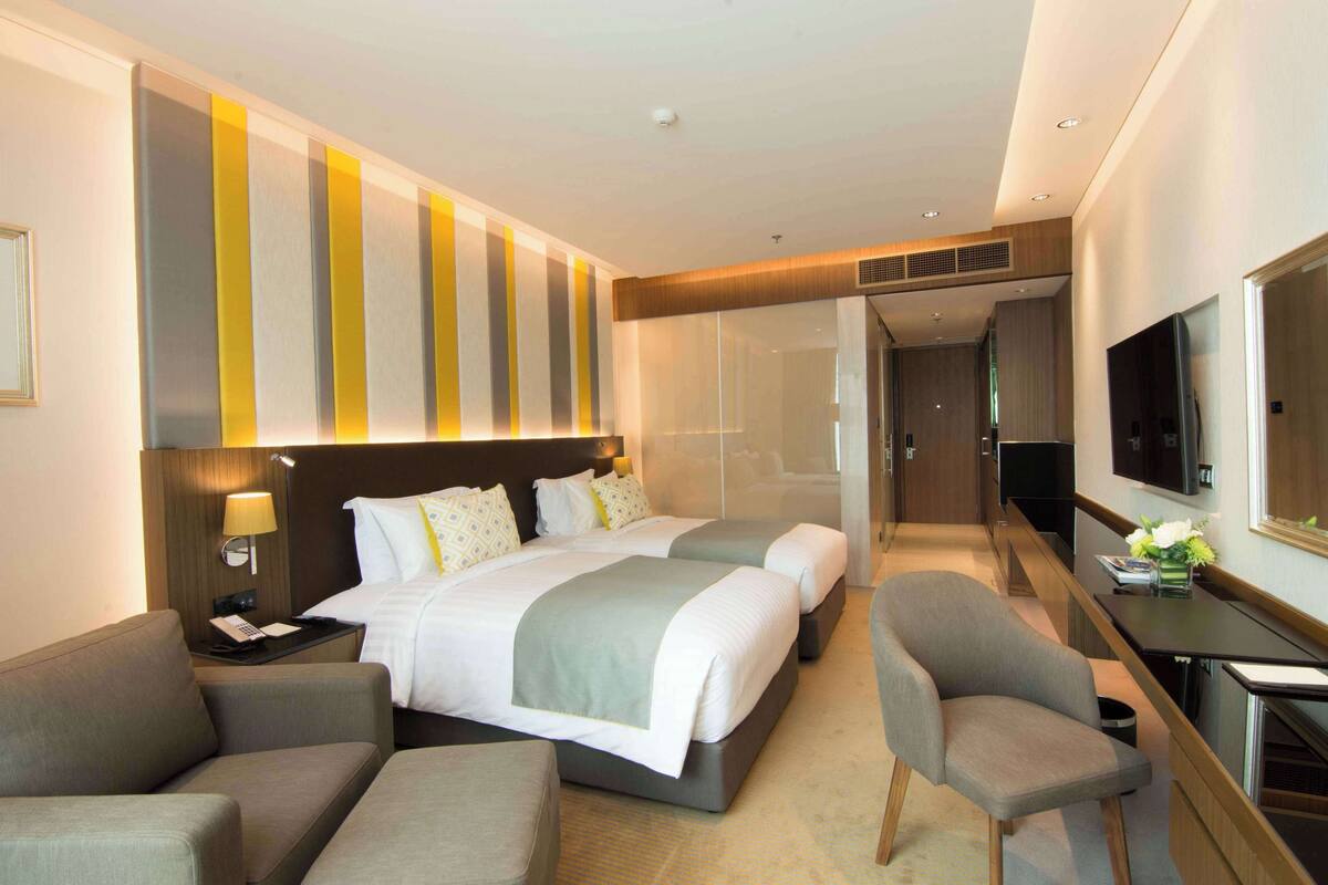 Een moderne hotelkamer met een groot bed, twee nachtkastjes, een bureau met stoel, een televisie en een grote spiegel.