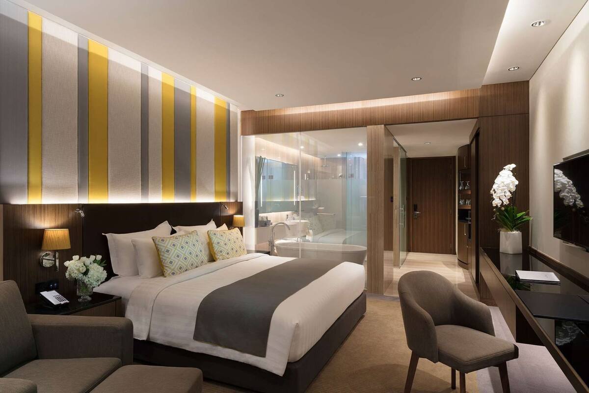 Een moderne hotelkamer met een groot bed, nachtkastjes, een bureau, een stoel, een televisie en een badkamer zichtbaar door een glazen wand.