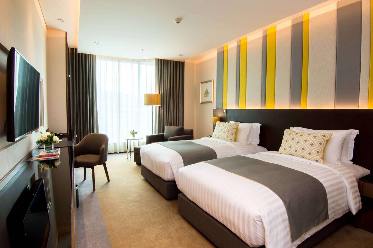 Een hotelkamer met twee bedden, een televisie, een bureau met een lamp en uitzicht op de omgeving.