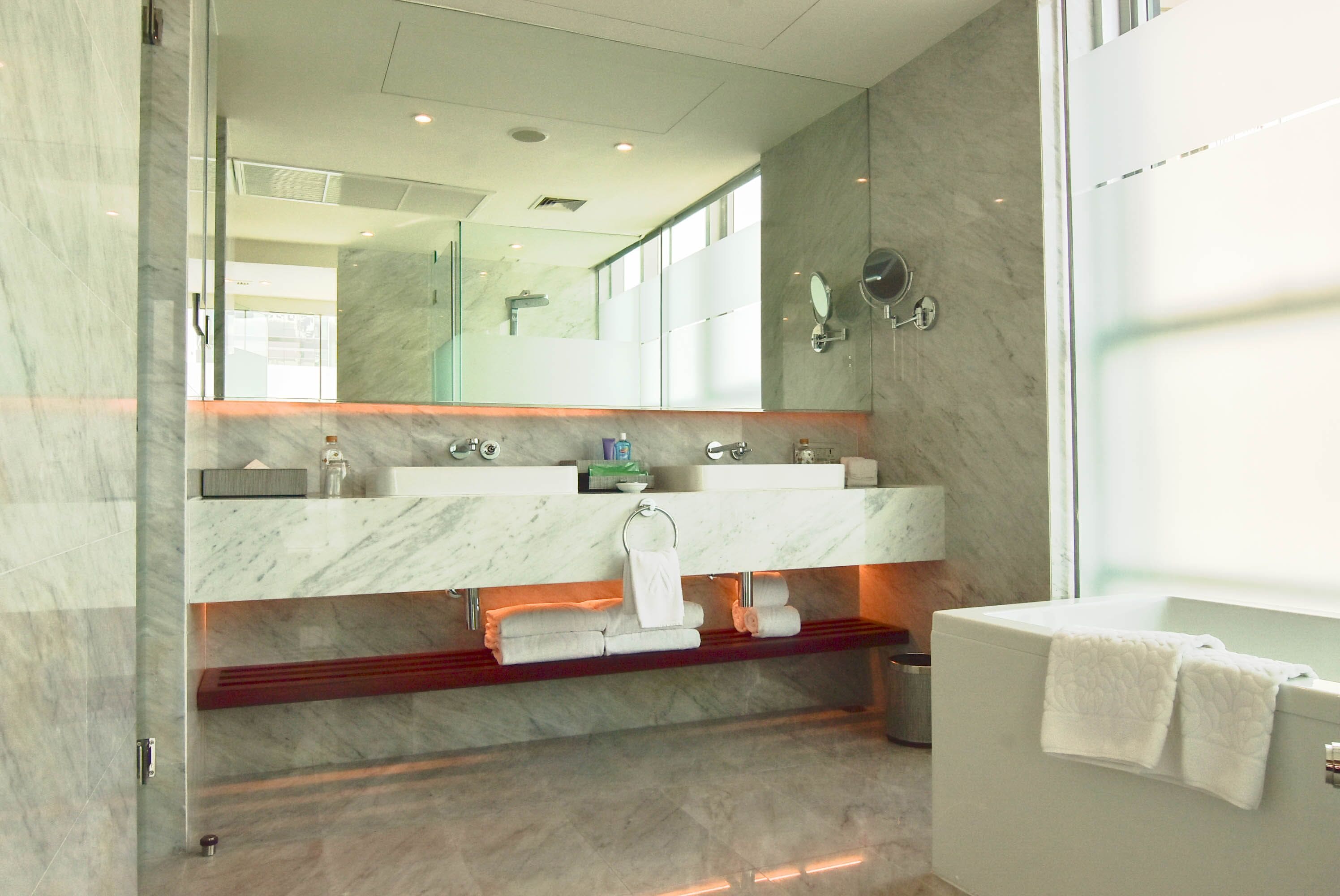 A modern bathroom with a marble vanity, dual sinks, a large mirror, and a bathtub.