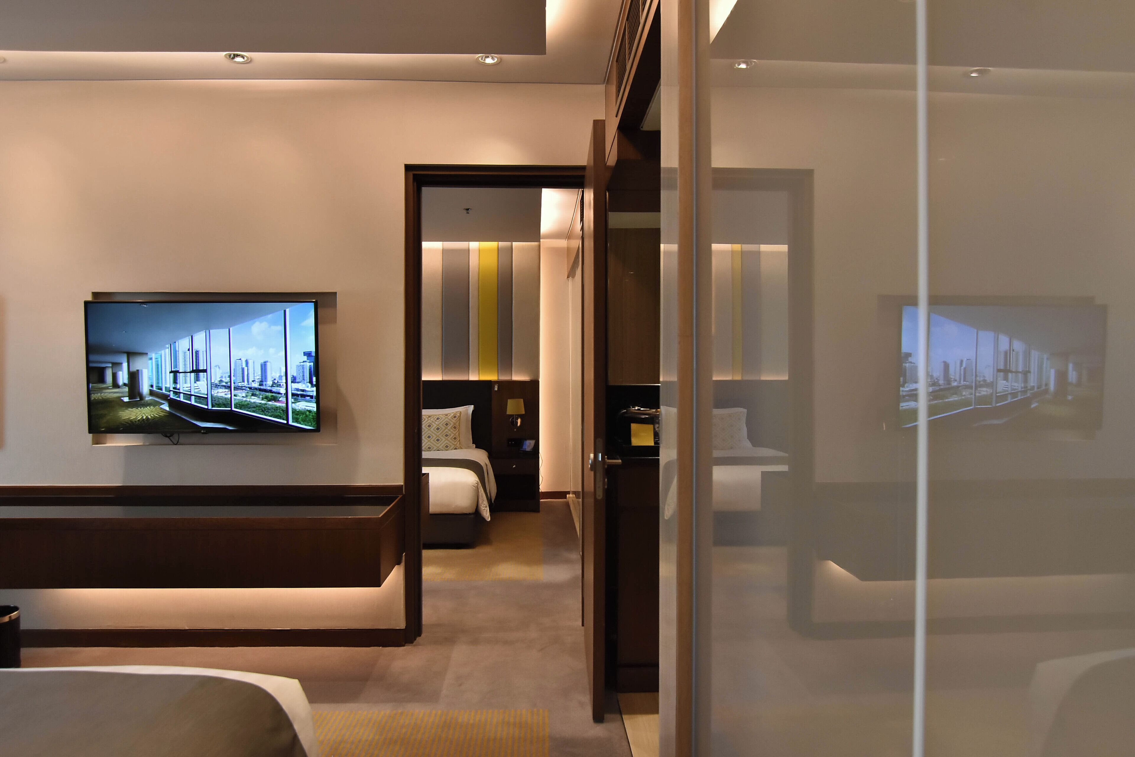 Et moderne hotelværelse med et stort fladskærms-tv ophængt på væggen, en seng med sengegavl, et natbord og en lille skriveplads.