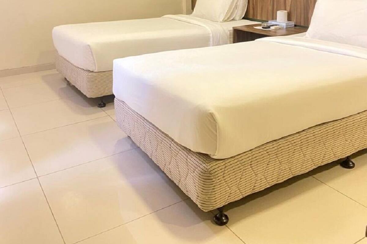 A hotel room with two beds, a wooden headboard, a green accent wall, and a small table with a lamp.