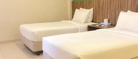 Habitación de hotel con dos camas individuales, cabecera de madera, una mesita con lámpara y una pared de acento verde.