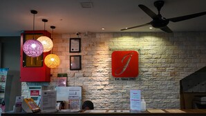 A hotel reception desk with a stone wall backdrop, a red logo, and a ceiling fan. - Hotel Jelai Raub (Raub)