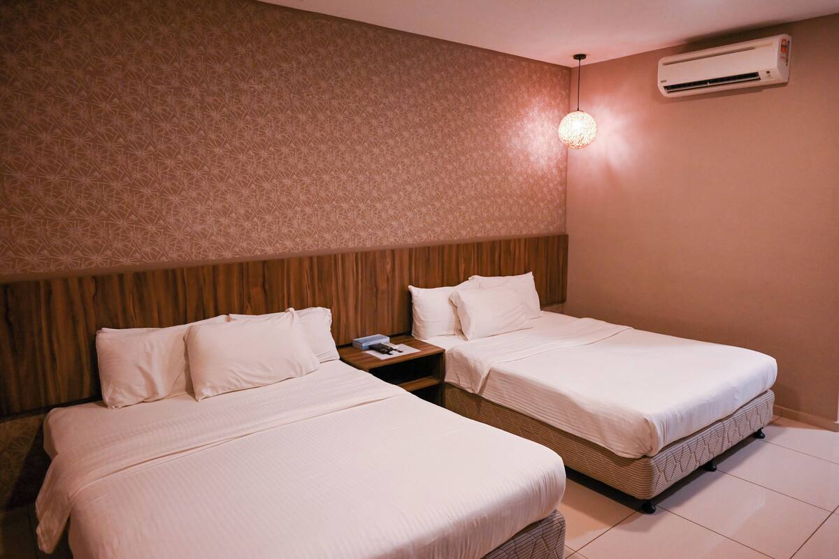 A hotel room with two beds, a wooden headboard, an air conditioning unit, and a nightstand with a lamp.