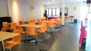 A cafeteria with orange chairs and tables, a painting on the wall, and a no-smoking sign. - Hotel Jelai Raub (Raub)