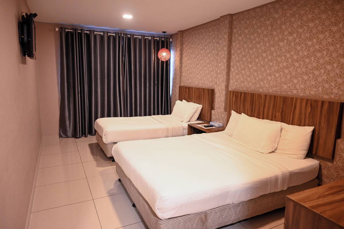 A hotel room with two beds, a wooden headboard, a nightstand, a remote control, and a patterned wall.
