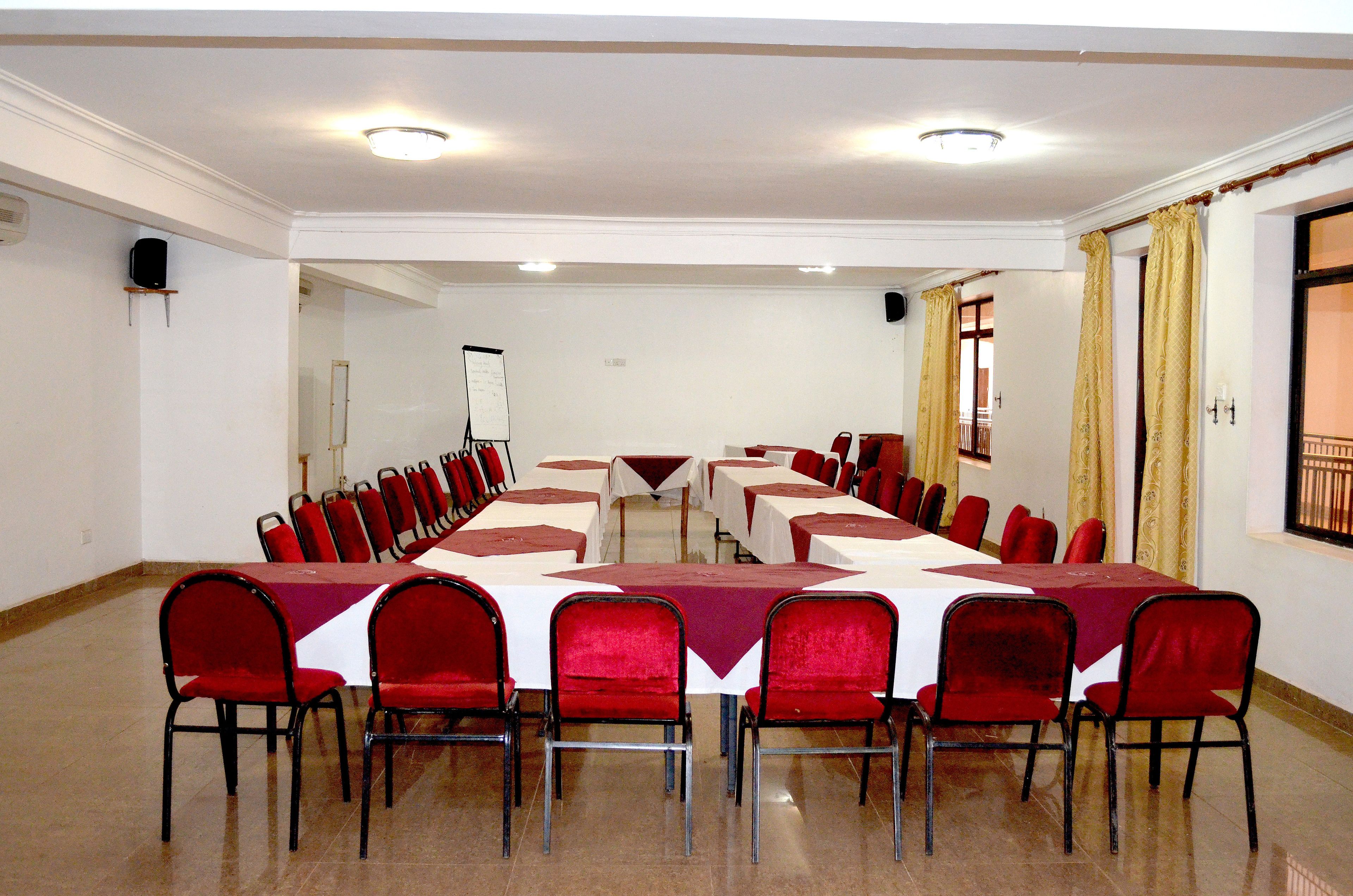 A conference room with a long table and red chairs, white walls, and a large window with curtains.