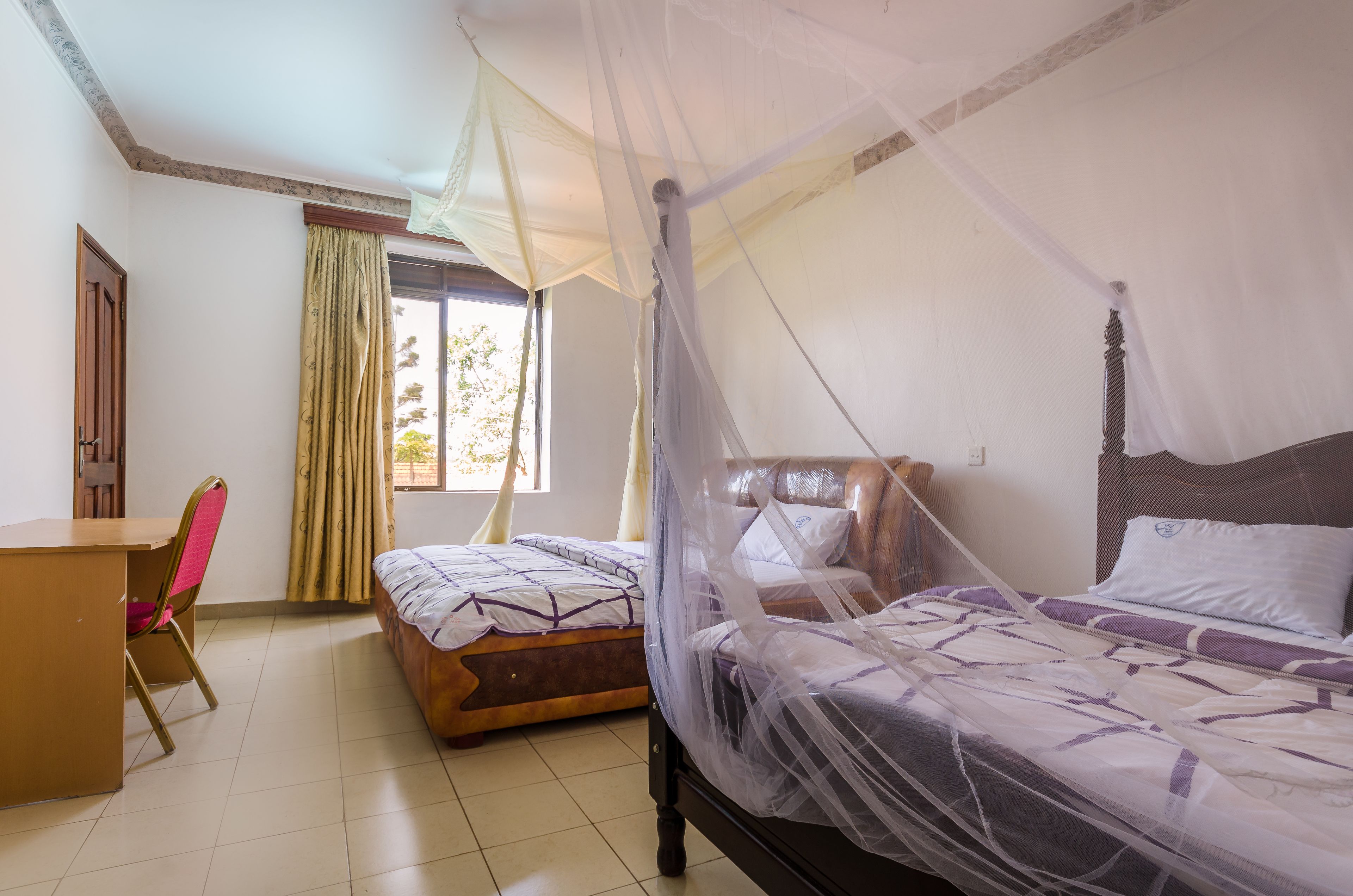 A room with two beds, one with a canopy, a desk, and a chair.