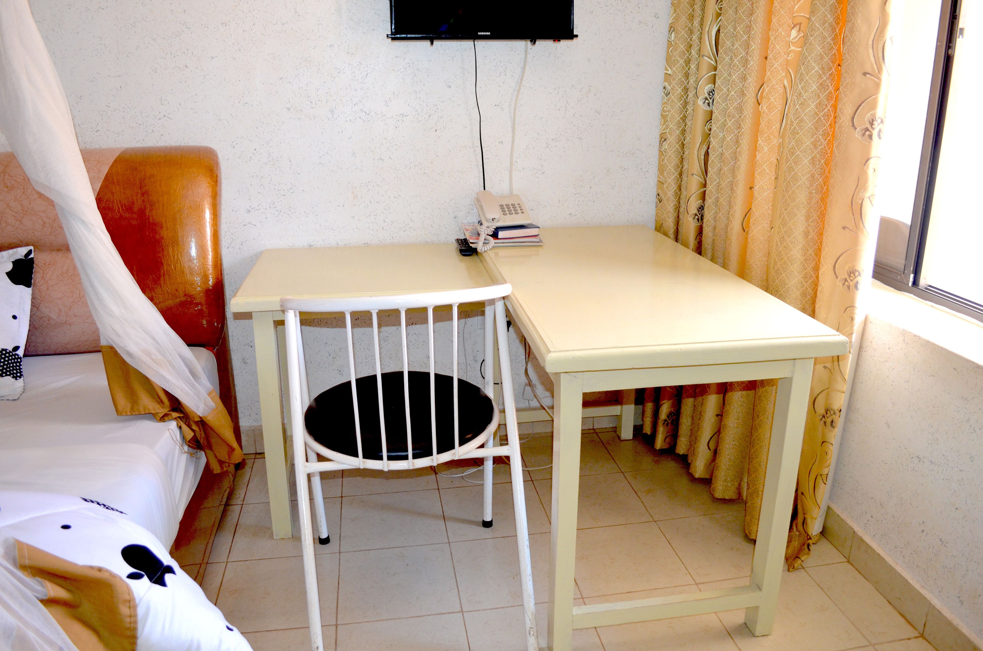 A small, simple room with a bed, a chair, a table, a telephone, and curtains.