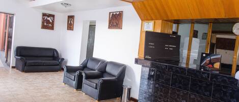 A reception area with a black leather sofa, a trash bin, and a reception desk with a digital display.