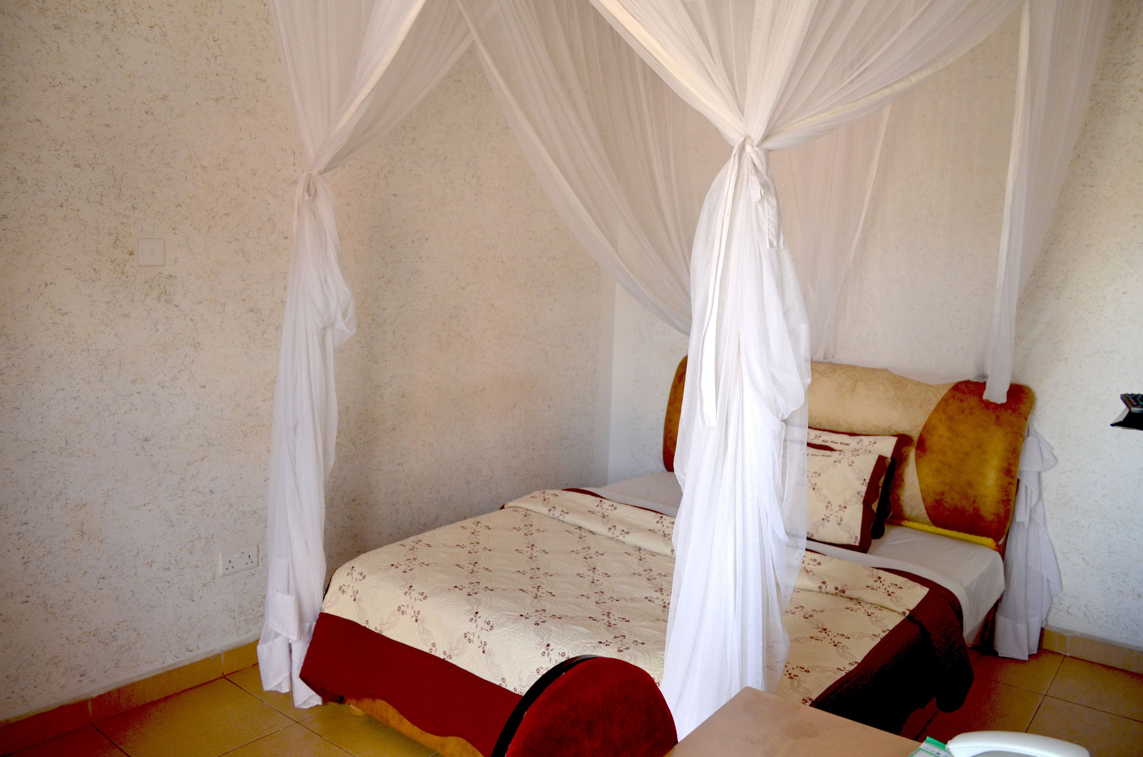 A single bed with a canopy, a bedside table, and a wall socket.