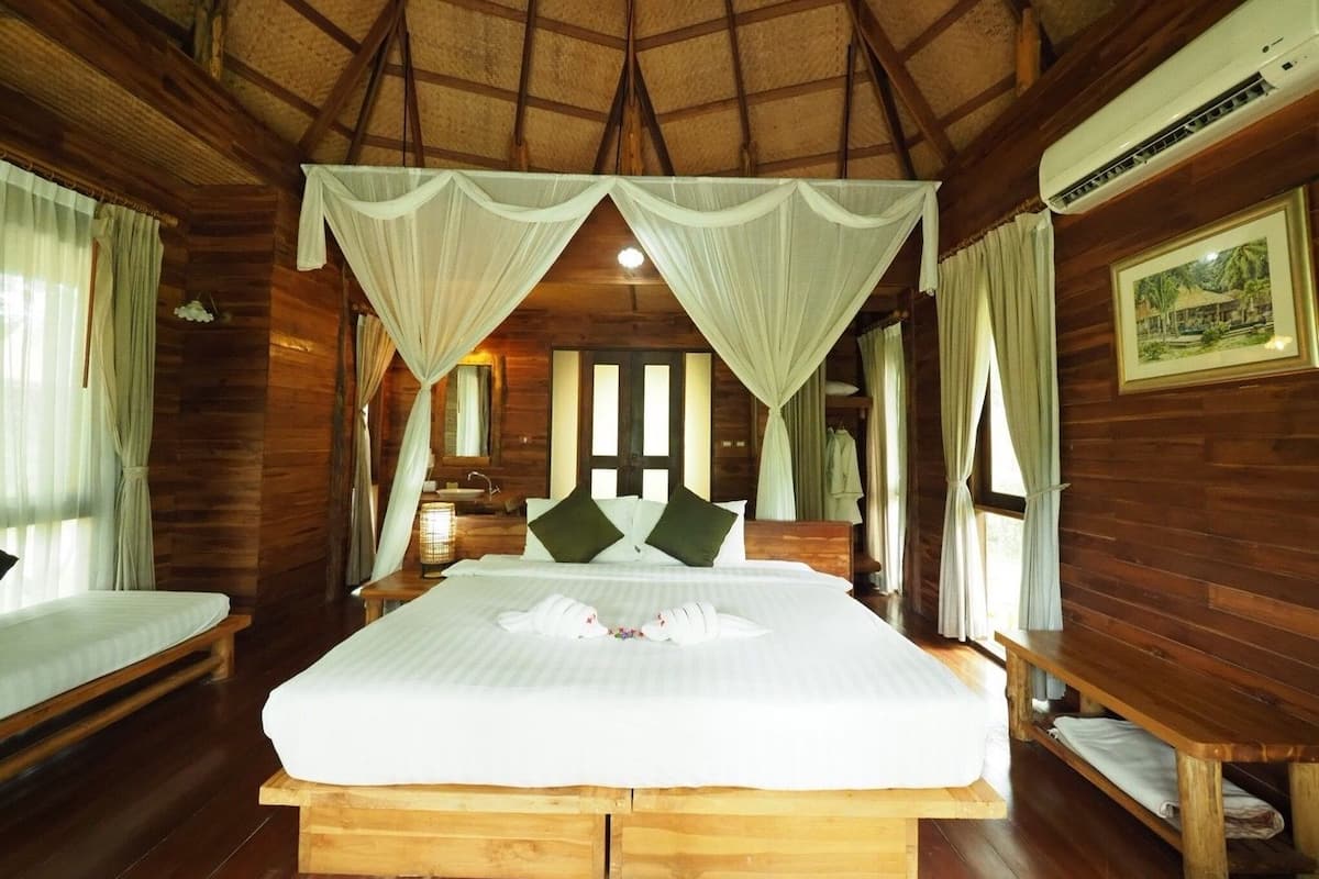 A wooden room with a large bed, a bench, a bedside table, a mirror, and a picture on the wall.