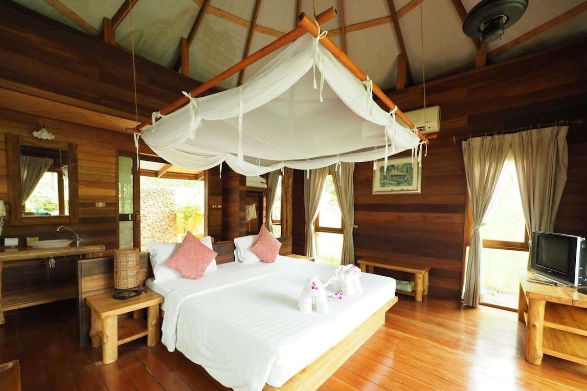 A wooden cabin bedroom with a bed, bedside tables, a TV, and a canopy bed.