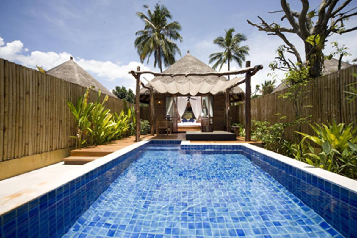 A swimming pool with a tiled blue surface, surrounded by a wooden fence and tropical plants.