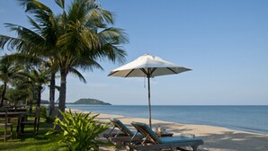 A beach with palm trees, lounge chairs, and a white umbrella. - Keeree Waree Seaside Villa (Bang Saphan)