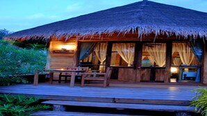 A wooden cabin with a thatched roof, wooden deck, and outdoor seating area. - Keeree Waree Seaside Villa (Bang Saphan)