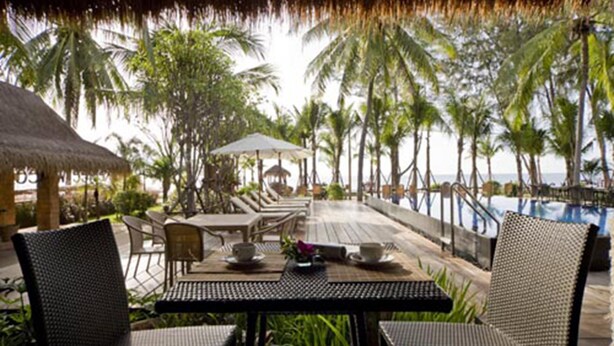 A poolside area with lounge chairs and tables, surrounded by palm trees and a view of the ocean. - Keeree Waree Seaside Villa (Bang Saphan)