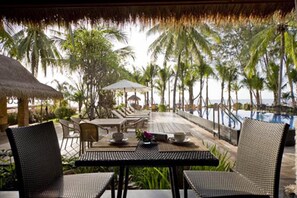 A poolside area with lounge chairs and tables, surrounded by palm trees and a view of the ocean. - Keeree Waree Seaside Villa (Bang Saphan)
