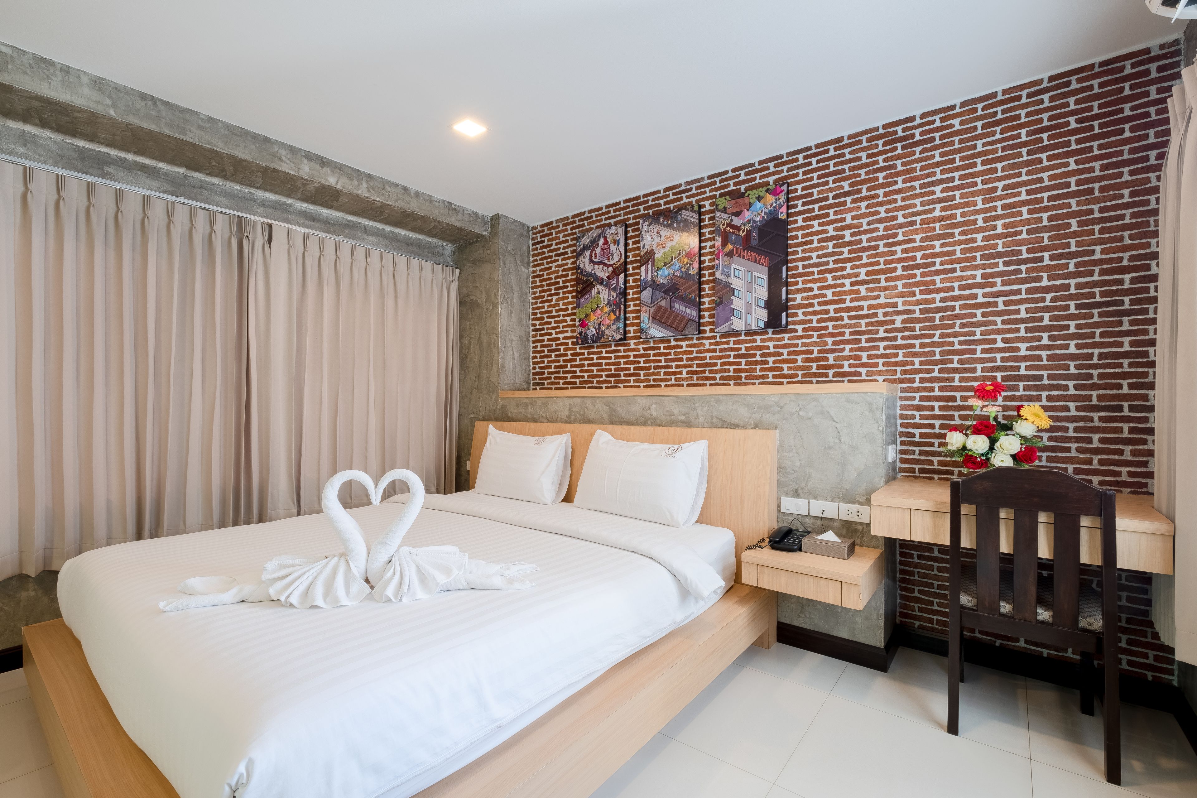Een hotelkamer met een bed, een bureau, een stoel en een bakstenen muur met kunstwerk.