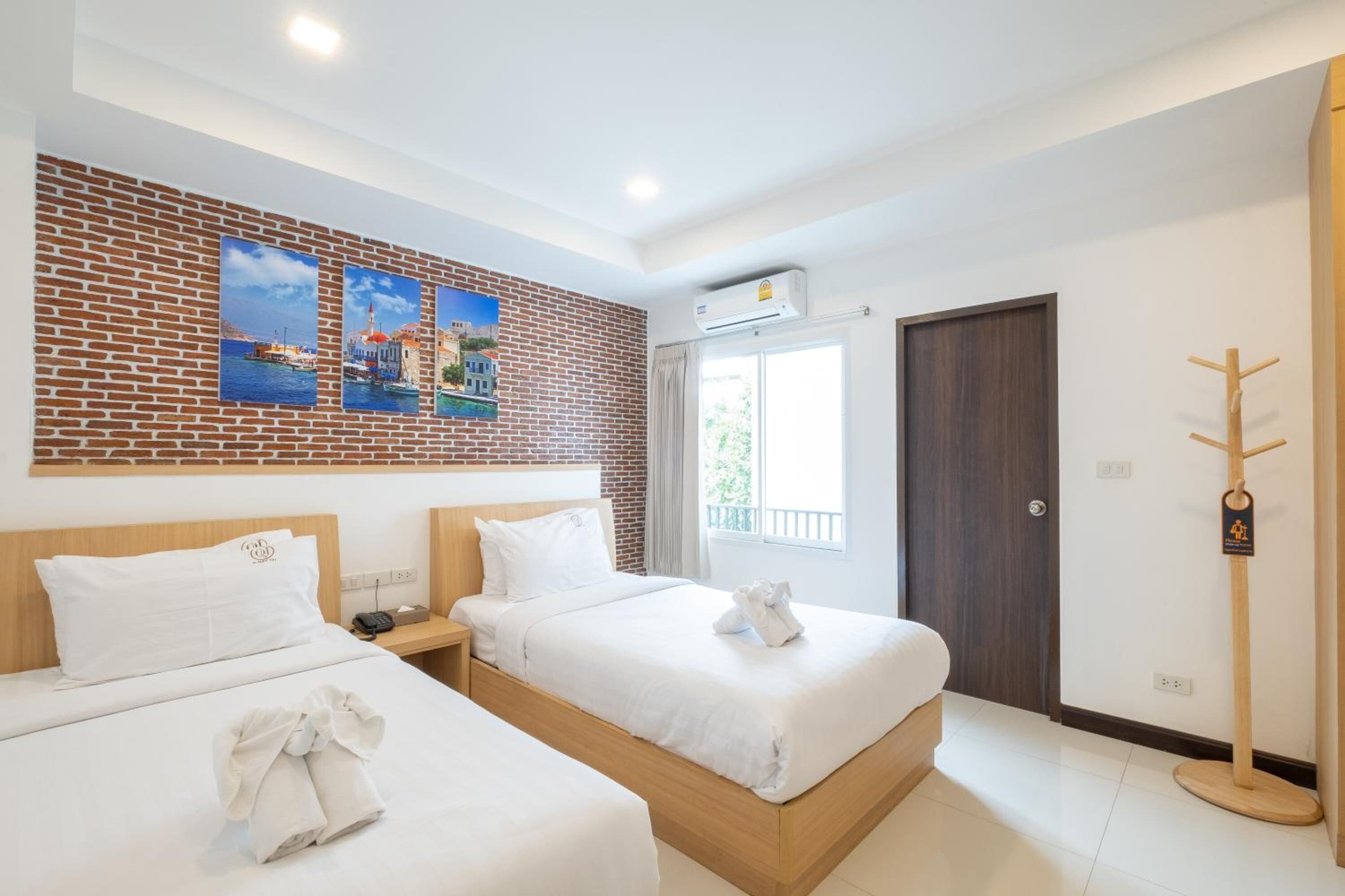 A hotel room with two beds, a brick-patterned wall, and a window with a view.
