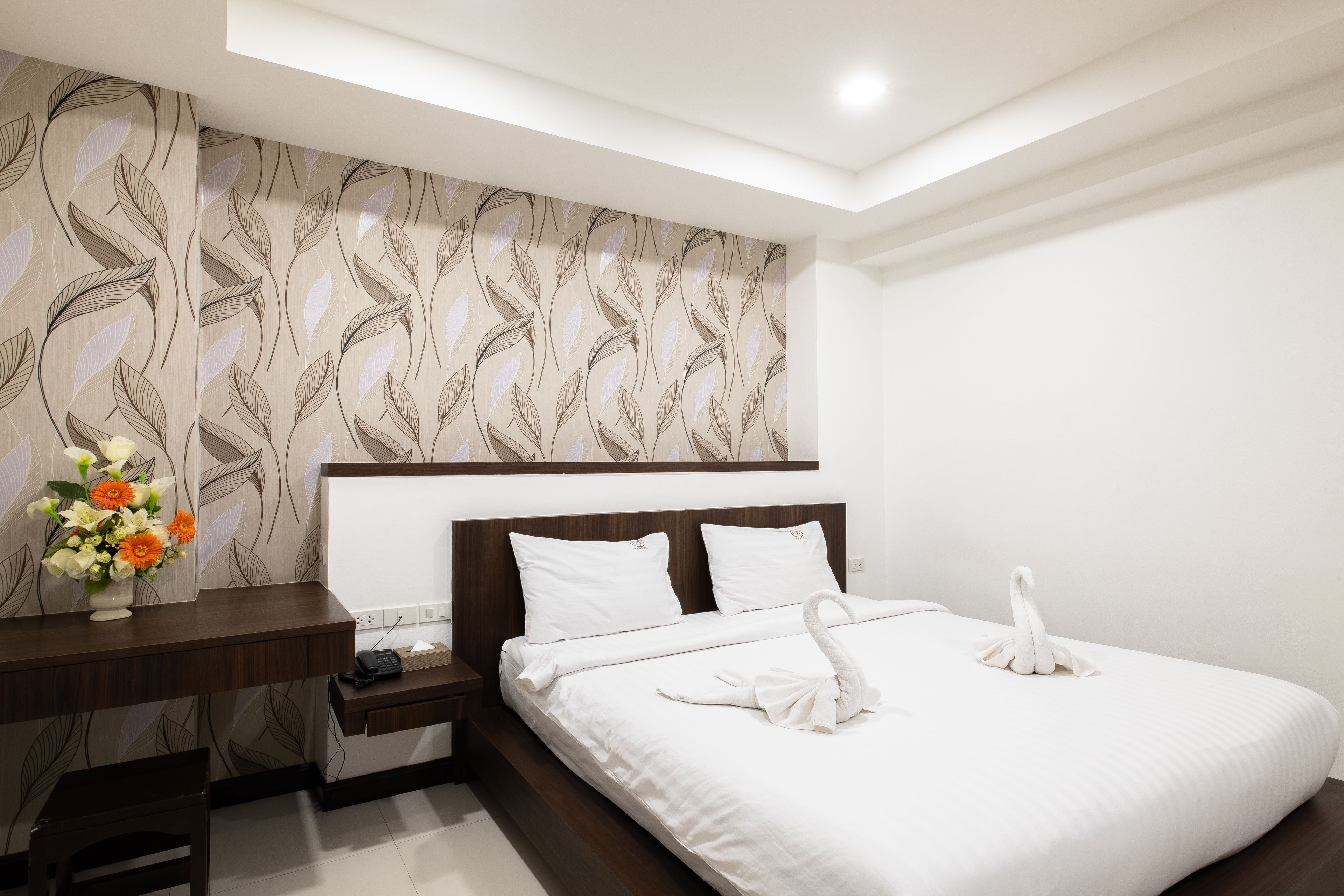 Une chambre d’hôtel avec un lit, un bureau et un mur orné d’un motif de feuilles.