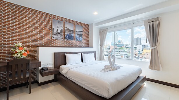 Una habitación de hotel moderna con pared de ladrillo, una cama grande con ropa blanca, un escritorio con teléfono y una ventana con vista a la ciudad.