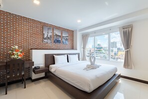A modern hotel room with a brick wall, a large bed with white linens, a desk with a telephone, and a window with a city view. - U Hatyai Hotel (Hat Yai)