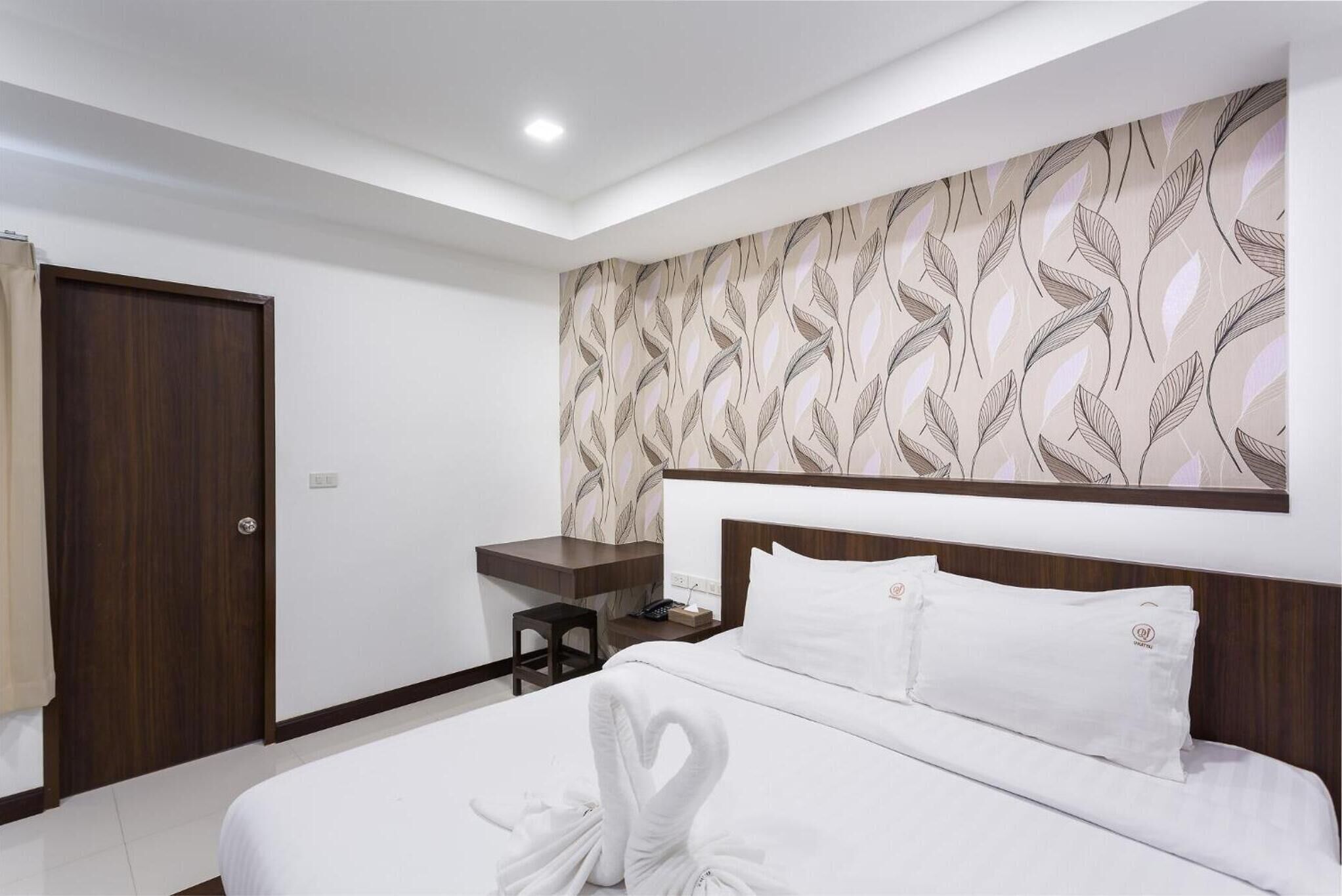 A hotel room with a neatly made bed, a wooden desk, and a patterned wallpaper.