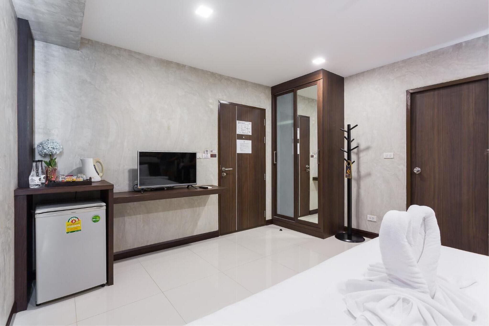 Une chambre d’hôtel équipée d’un lit, d’une télévision, d’un petit réfrigérateur, d’un miroir et d’un porte-manteau.