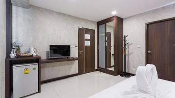 Une chambre d’hôtel équipée d’un lit, d’une télévision, d’un petit réfrigérateur, d’un miroir et d’un porte-manteau.