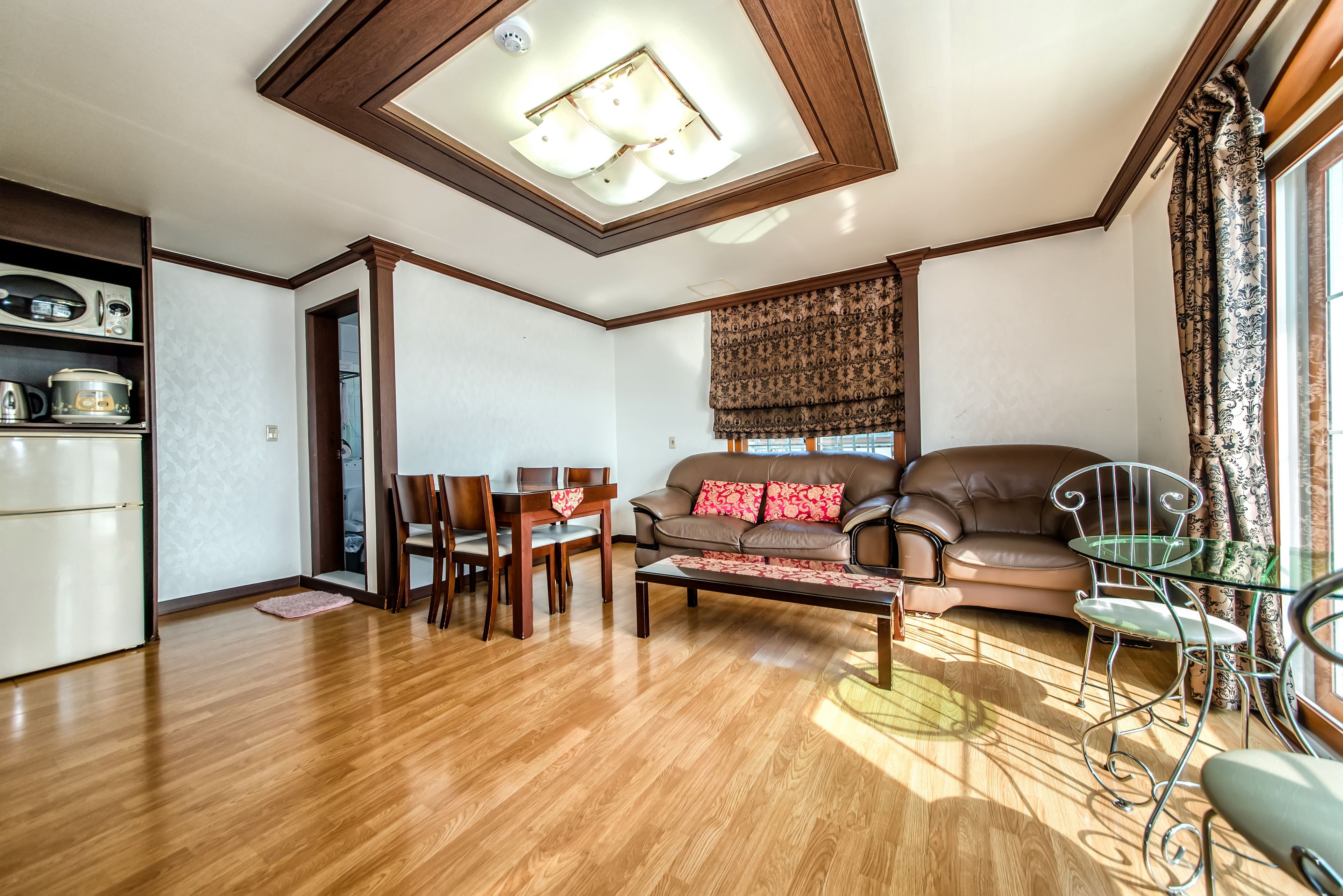Una sala de estar con piso de madera, un sofá de cuero marrón, una mesa de comedor con sillas y una mesa de centro de vidrio.