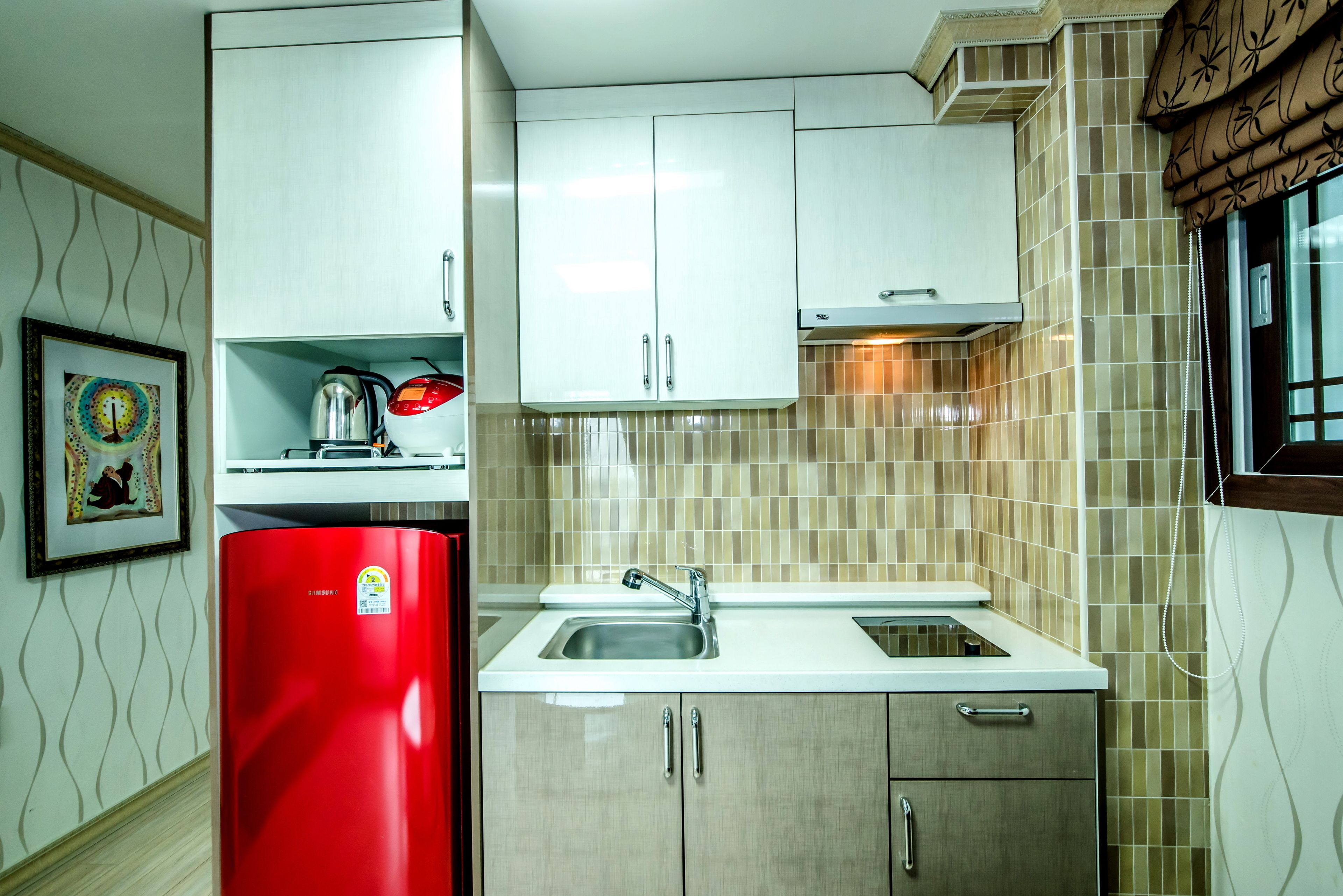 A compact kitchen with white cabinets, a red refrigerator, and a tiled backsplash.