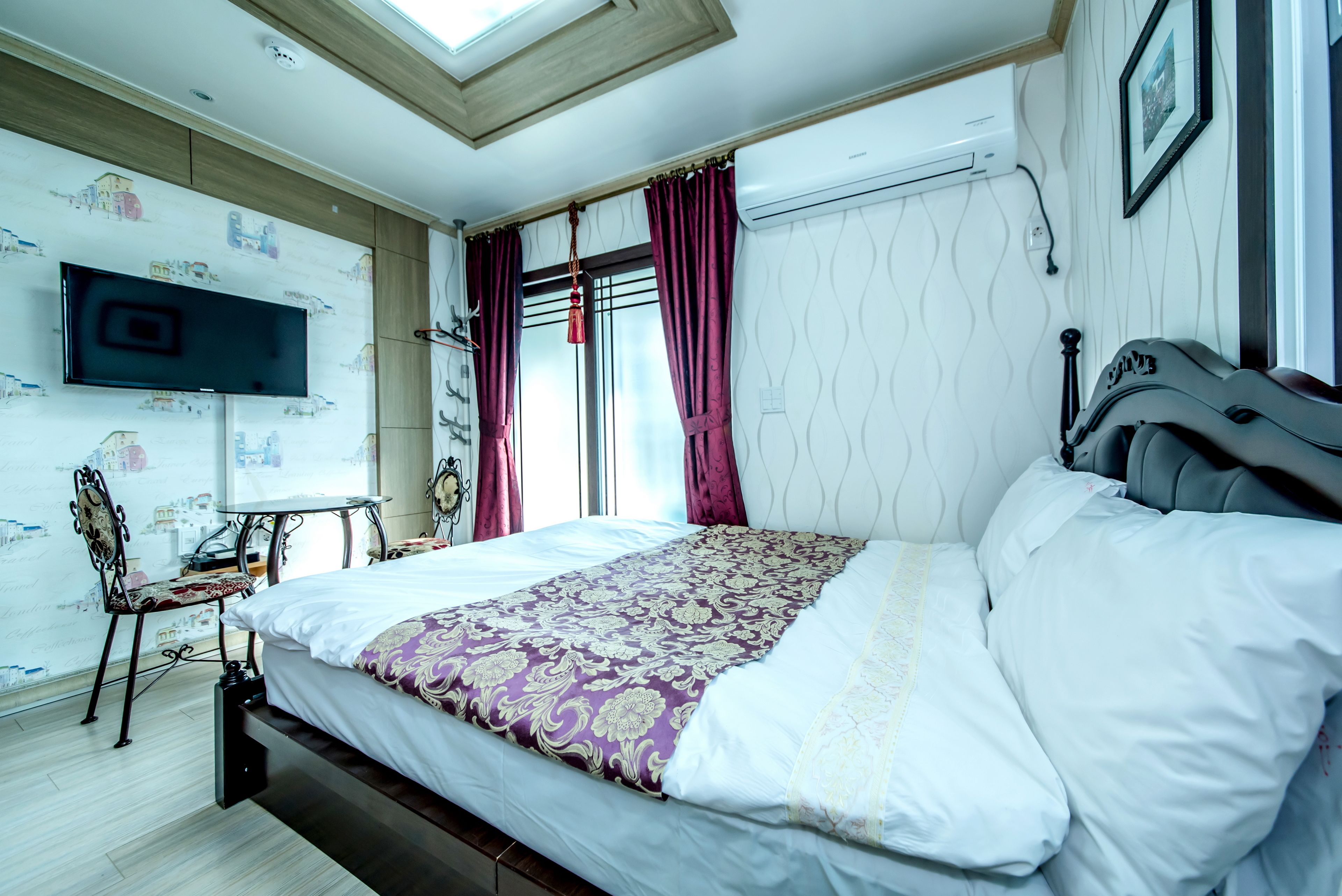 A bedroom with a bed, a TV mounted on the wall, a desk, and a chair.
