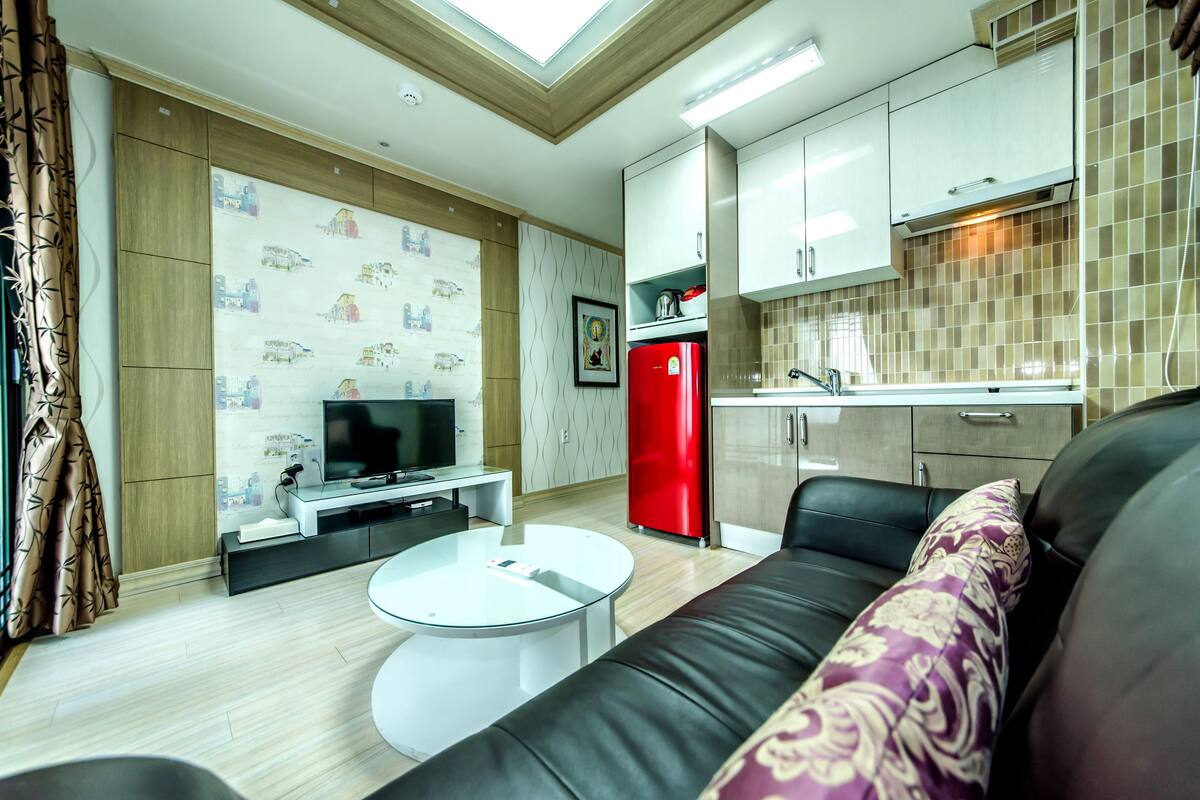 Un salon moderne avec un canapé, une table basse, un téléviseur et un réfrigérateur rouge.