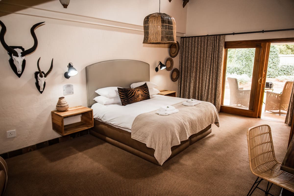 Une chambre spacieuse avec un grand lit, une table de chevet en bois, une lampe en osier et une chaise.