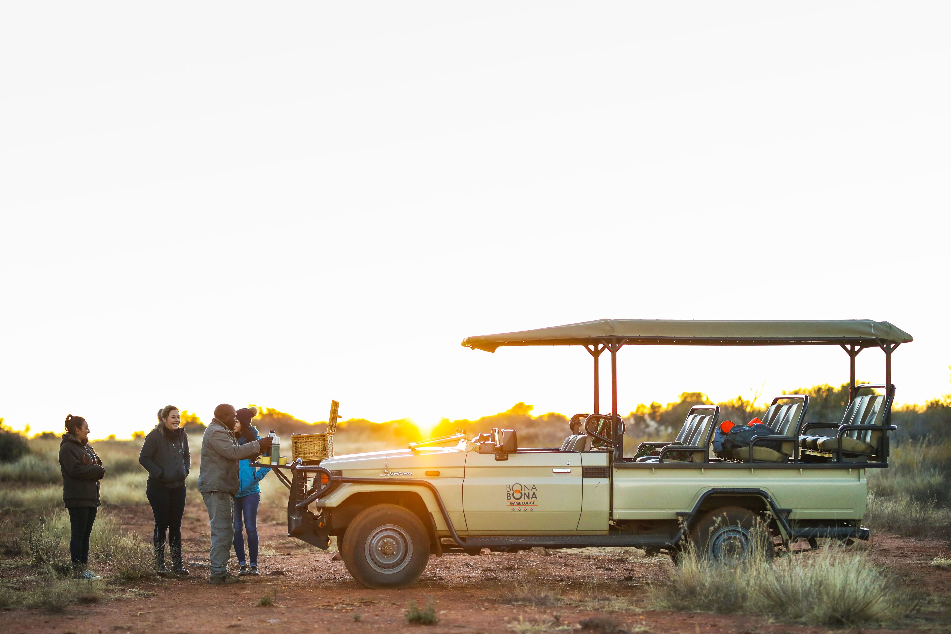 A safari vehicle with a canopy, parked on a dirt road with people standing nearby.