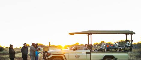 A safari vehicle with a canopy, parked on a dirt road with people standing nearby.